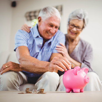 Smiling retired couple putting money in piggy bank